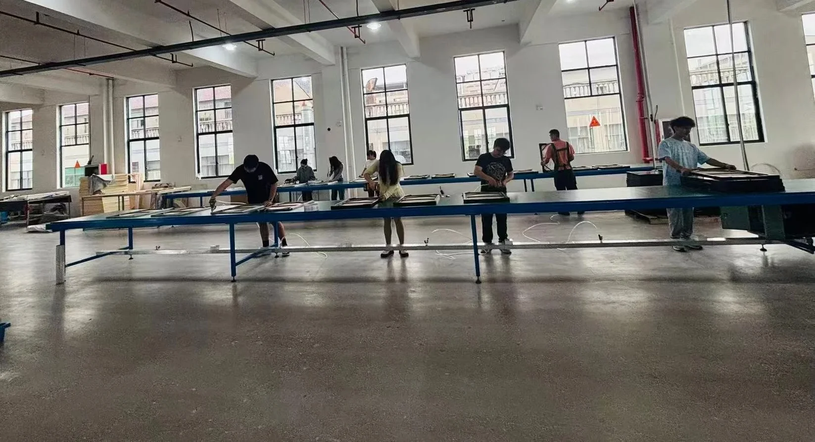 Production workers assembling framed wall art along a long bench
